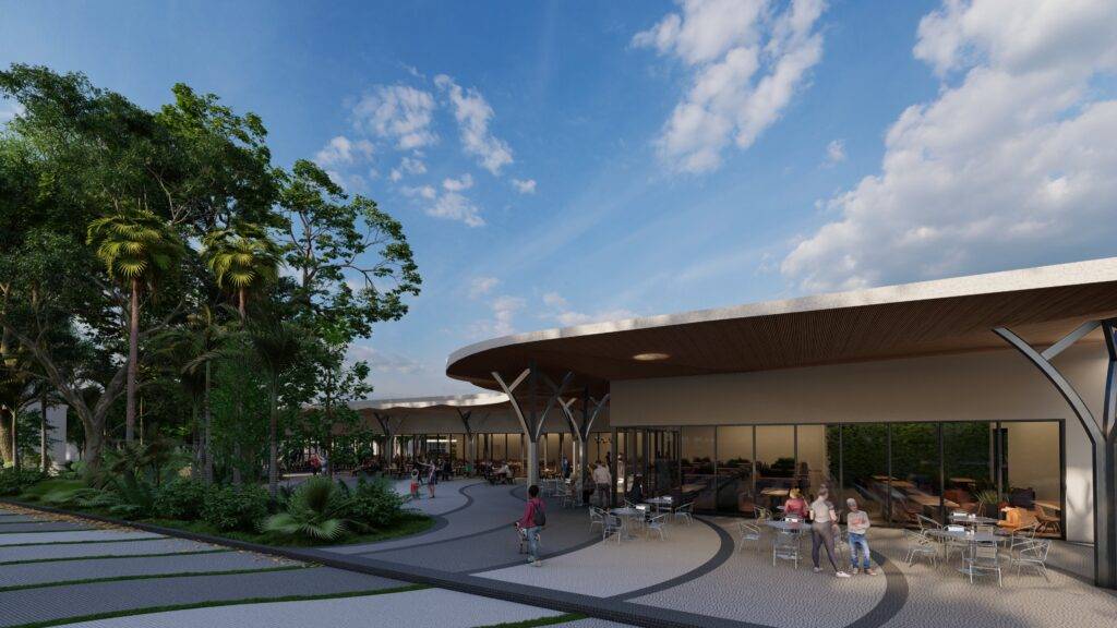 A modern architectural building with a curved roof and outdoor seating area surrounded by trees under a blue sky.