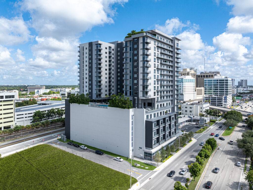 Aerial view of a modern high-rise building with blue skies and surrounding urban landscape.