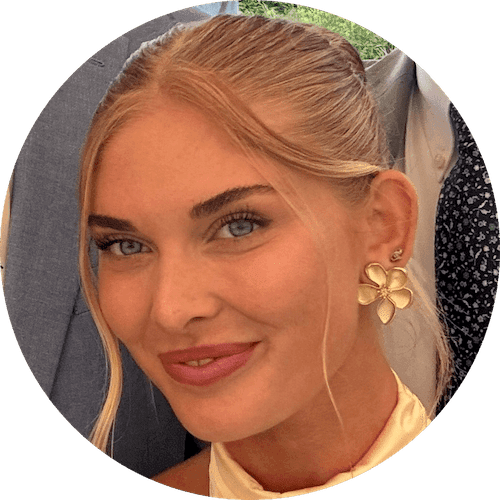 Smiling woman with light hair and floral earrings, wearing a light yellow top.