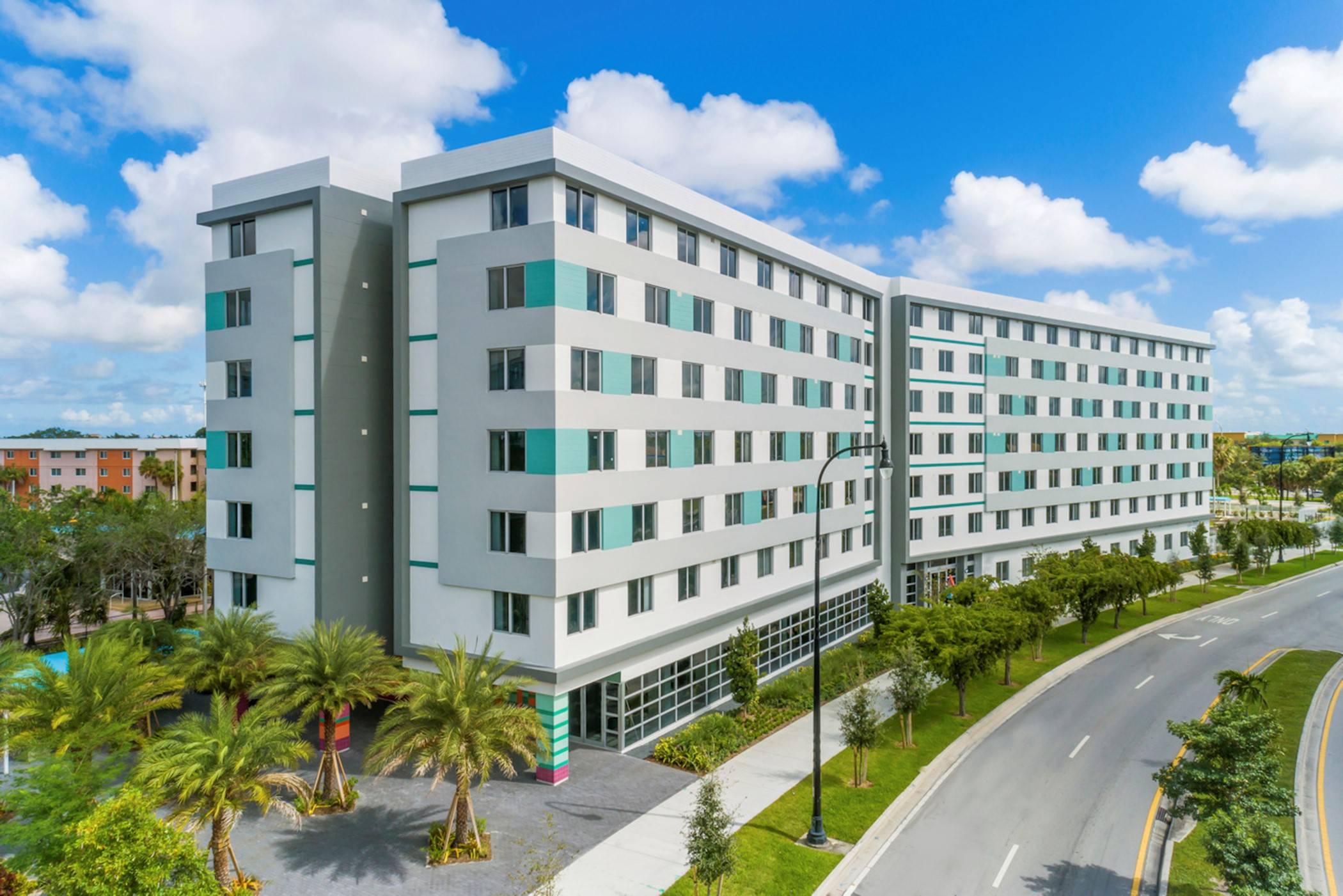 Modern multi-story building surrounded by lush greenery and palm trees on a sunny day.
