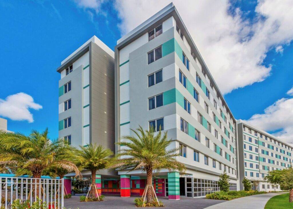 Modern six-story building with vibrant colors and palm trees against a blue sky.