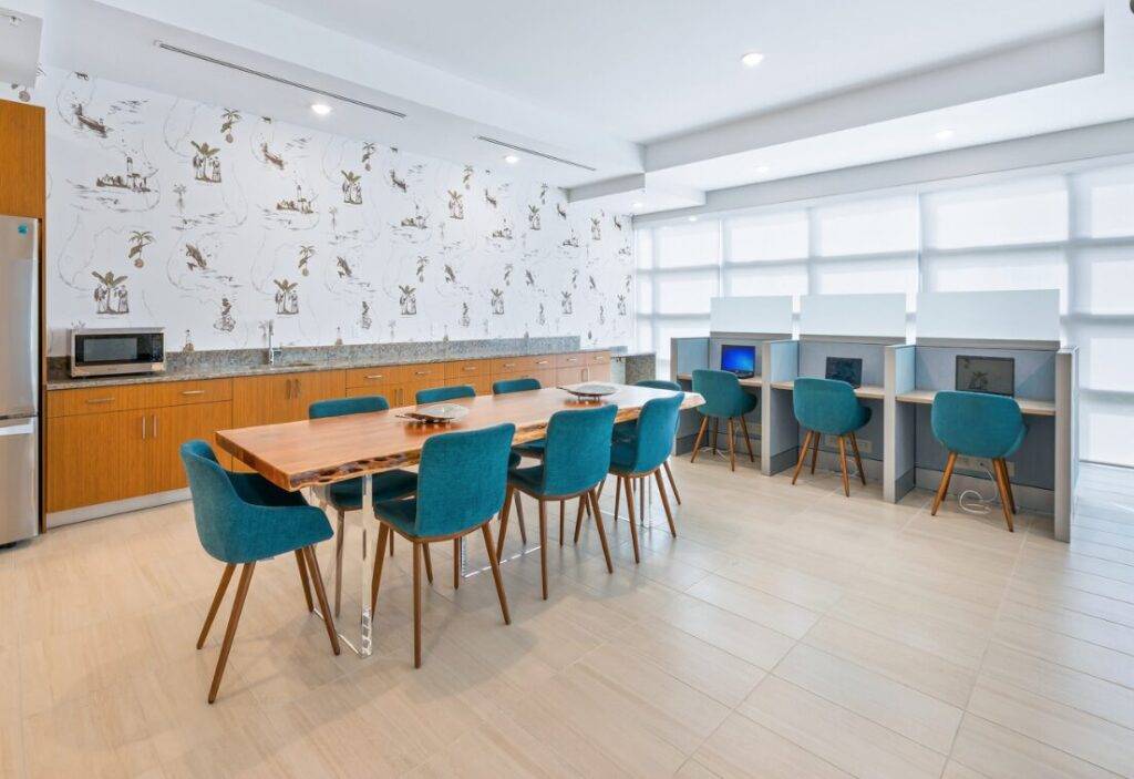 Modern communal workspace with wooden tables and teal chairs beneath bright lighting.