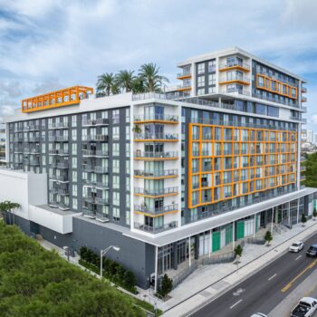 Modern multi-story building with orange accents and lush greenery in an urban setting.
