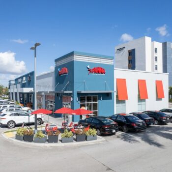 Vibrant shopping center with colorful storefronts and ample parking under a clear blue sky.