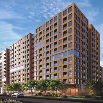 Modern brick apartment complex against a bright blue sky with greenery in the foreground.