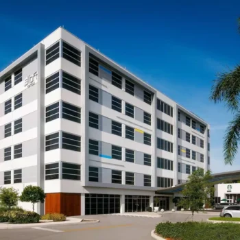 Modern office building with palm trees and a clear blue sky.