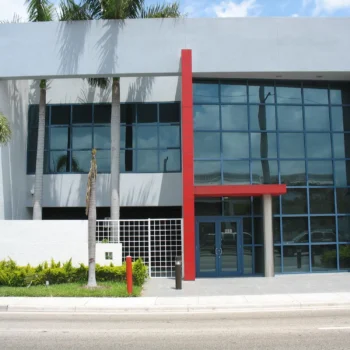 Modern commercial building with large glass windows and a bold red accent feature, set against a clear sky.