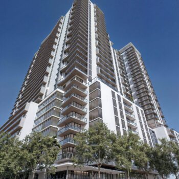 Modern high-rise building with glass balconies against a clear blue sky.
