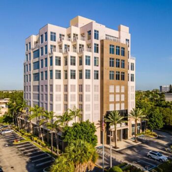 Aerial view of a modern multi-story office building surrounded by palm trees on a sunny day.