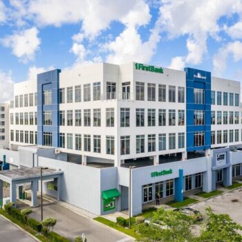 Modern office building with white and blue facade under a bright blue sky.