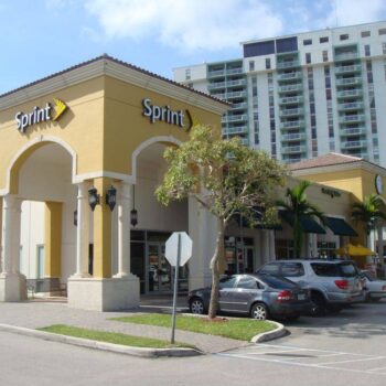 A Sprint store in a modern yellow building with arches, located in a bustling city area with high-rise apartments in the background.