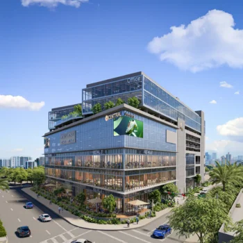 Modern multi-story office building with glass facade against a clear blue sky, surrounded by lush greenery in an urban setting.