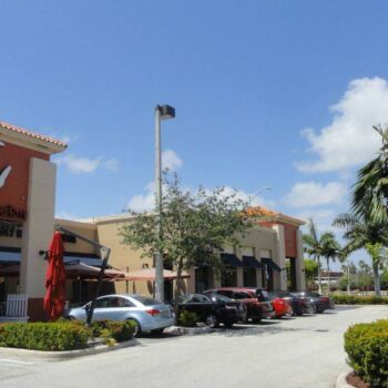 Shopping plaza with cars parked in front on a sunny day.