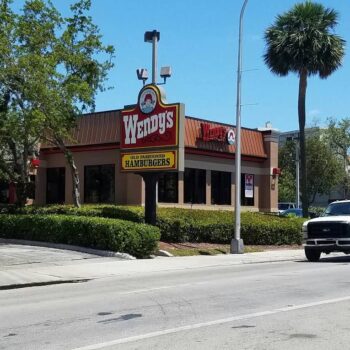 Wendy's restaurant with classic logo on a sunny day, surrounded by lush greenery and palm trees.