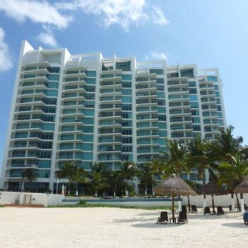 Modern beachfront condominium with palm trees and loungers under a clear blue sky.