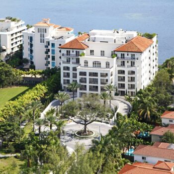 Aerial view of a luxurious waterfront residential building with terracotta roofs surrounded by lush greenery.