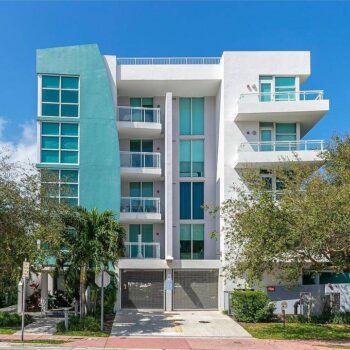 Modern white and turquoise apartment building with balconies and lush greenery.