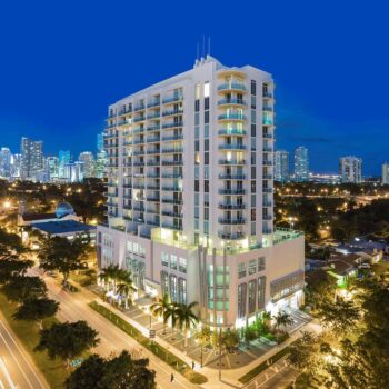 Night view of an illuminated modern high-rise building amid a vibrant cityscape.
