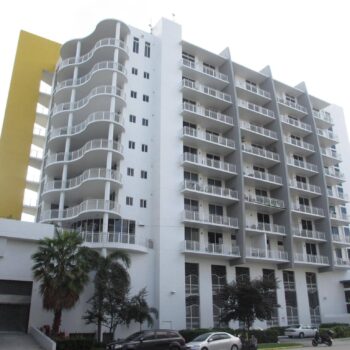 Modern white apartment building with balconies and a yellow side panel.