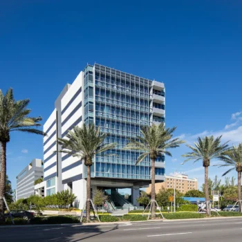 Modern office building with palm trees under a clear blue sky.
