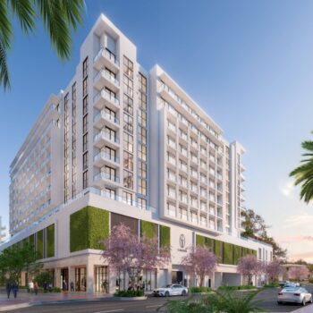 Modern luxury hotel building with lush greenery and clear blue sky.