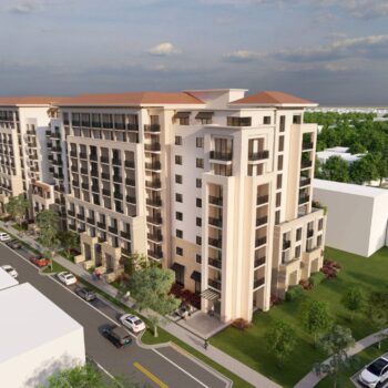 Aerial view of a modern multi-story residential building with lush green surroundings and a bustling street.