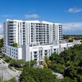 Luxurious high-rise apartment building surrounded by lush greenery under a clear blue sky.