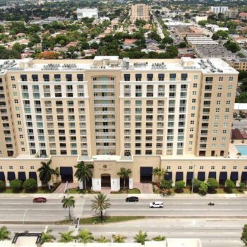Aerial view of a large residential building with palm trees and a surrounding urban landscape.