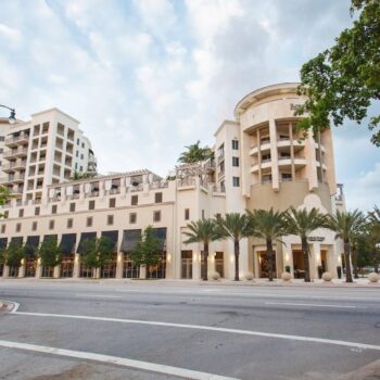 Elegant multi-story building with palm trees and a cloudy sky.
