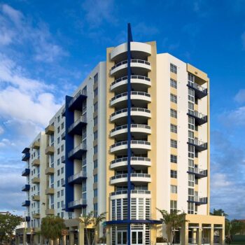 Modern high-rise apartment building with balconies and blue accents under a vibrant sky.