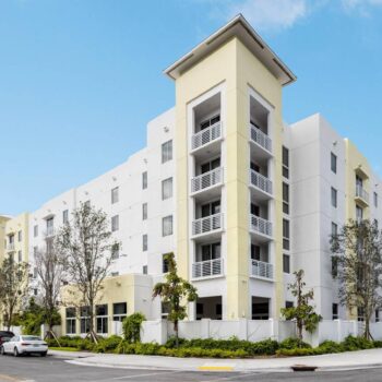Modern five-story residential building with balconies and lush greenery.