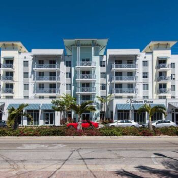 Modern white and glass apartment building with palm trees lining the front, under a clear blue sky.