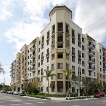 Modern urban apartment building with balconies and palm trees.