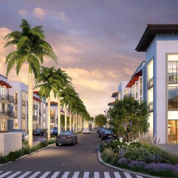 Modern apartment complex with palm trees lining a vibrant street at sunset.