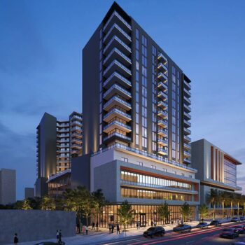 Modern urban residential building with illuminated windows and bustling street at dusk.