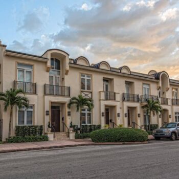 Elegant townhouses with palm trees and a car at sunset