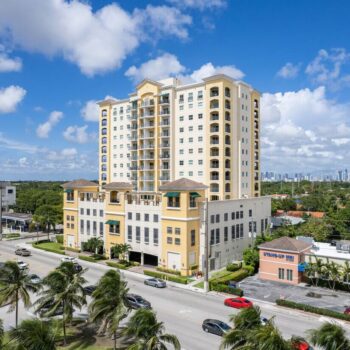 Modern apartment building with palm trees and a vibrant cityscape background.