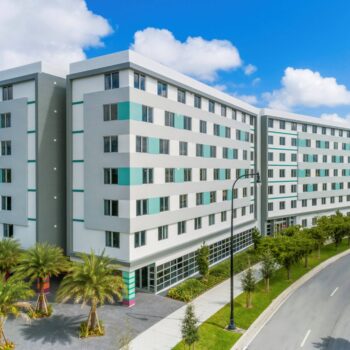 Modern multi-story building surrounded by lush greenery and palm trees on a sunny day.