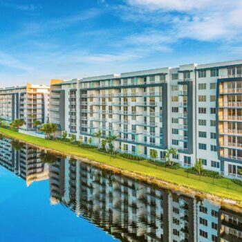 Modern waterfront apartment buildings with a clear blue sky reflected in a calm canal.