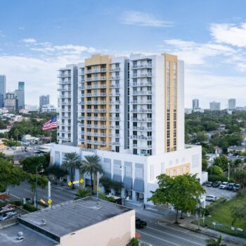 Aerial view of a modern city building with a backdrop of skyscrapers and lush greenery.