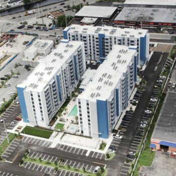 Aerial view of modern residential apartment complex with blue accents and parking area.